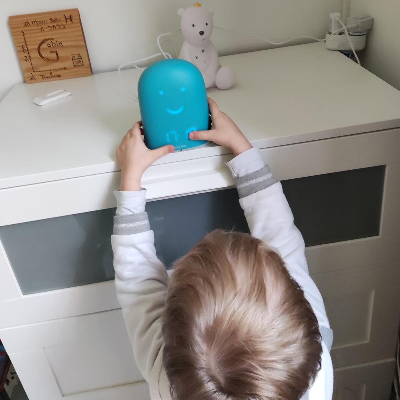 A child places a blue device on a white dresser in a neatly organized room.