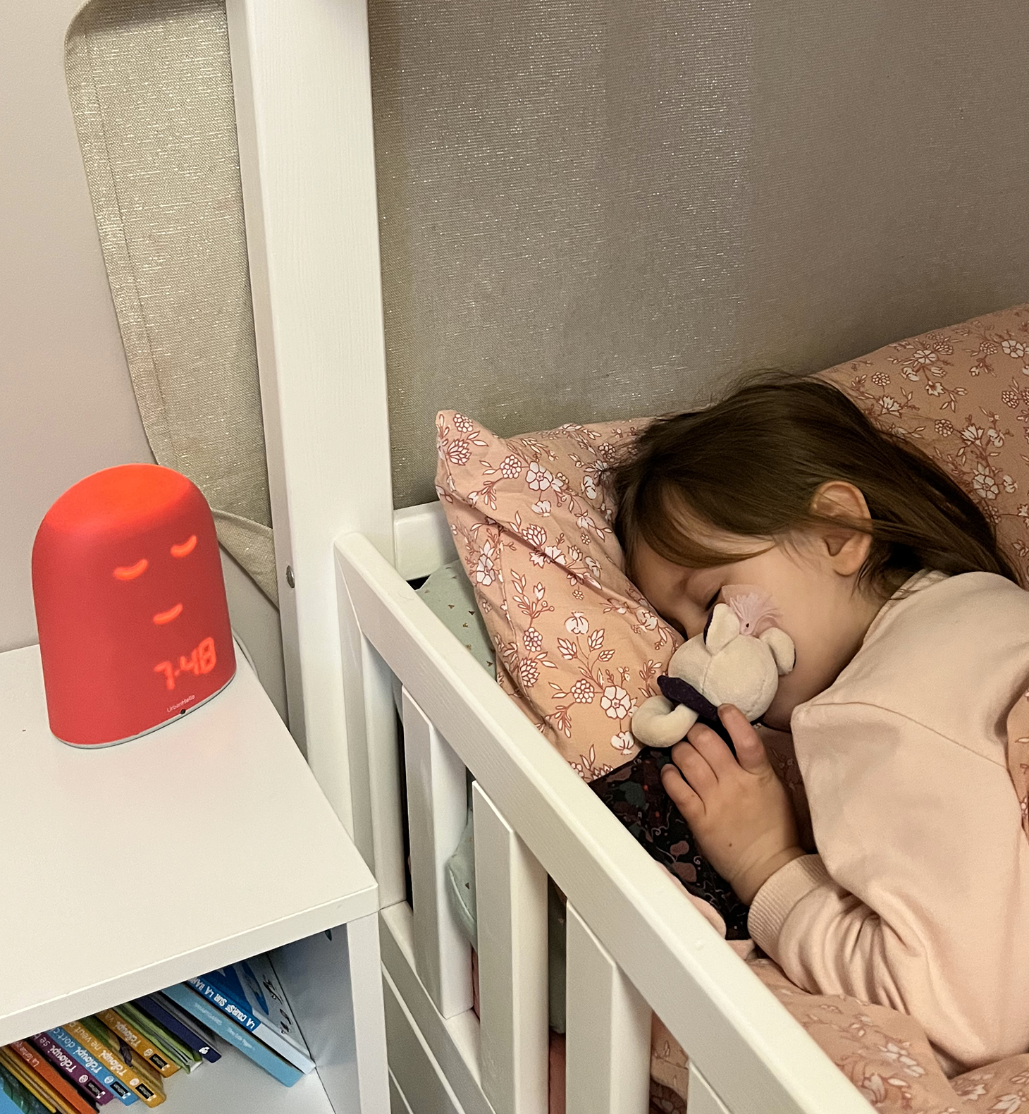 Une enfant dorment dans son lit près d’une veilleuse rouge sur la table de chevet.