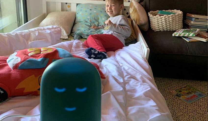 Image montrant un enfant assis sur un lit en train de sourire, avec une veilleuse bleue au premier plan dans sa chambre.